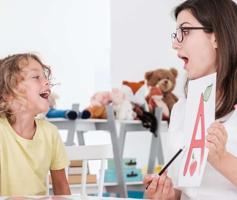 ABA therapist holding letter flashcard while a child with autism practices communication skills
