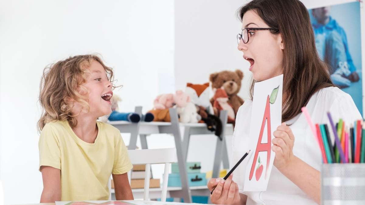 ABA therapist holding letter flashcard while a child with autism practices communication skills