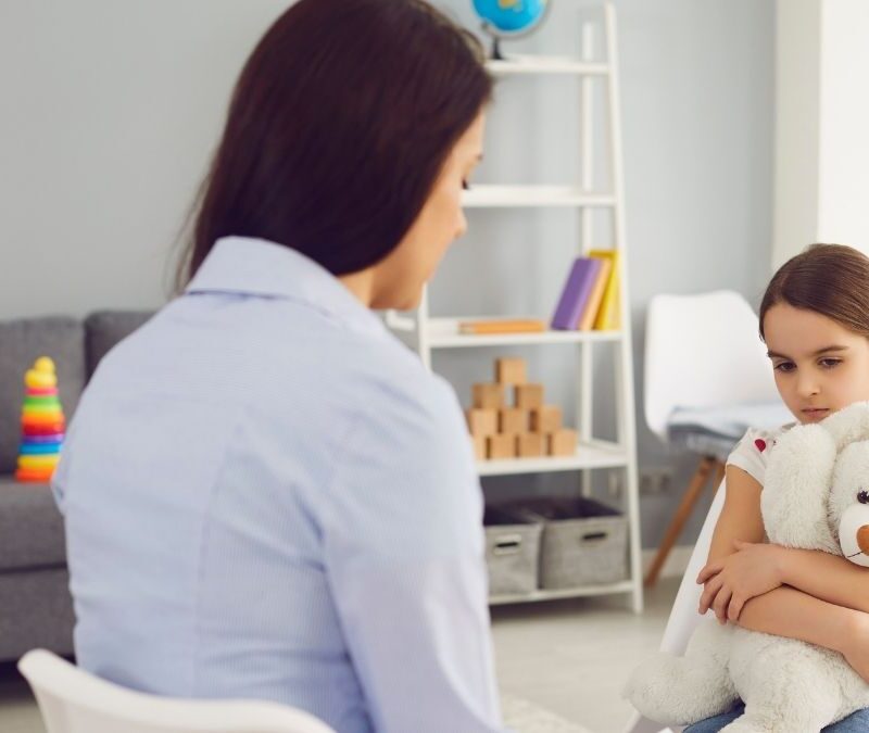 ABA therapist in NJ sitting with a young girl holding a teddy bear during a therapy session