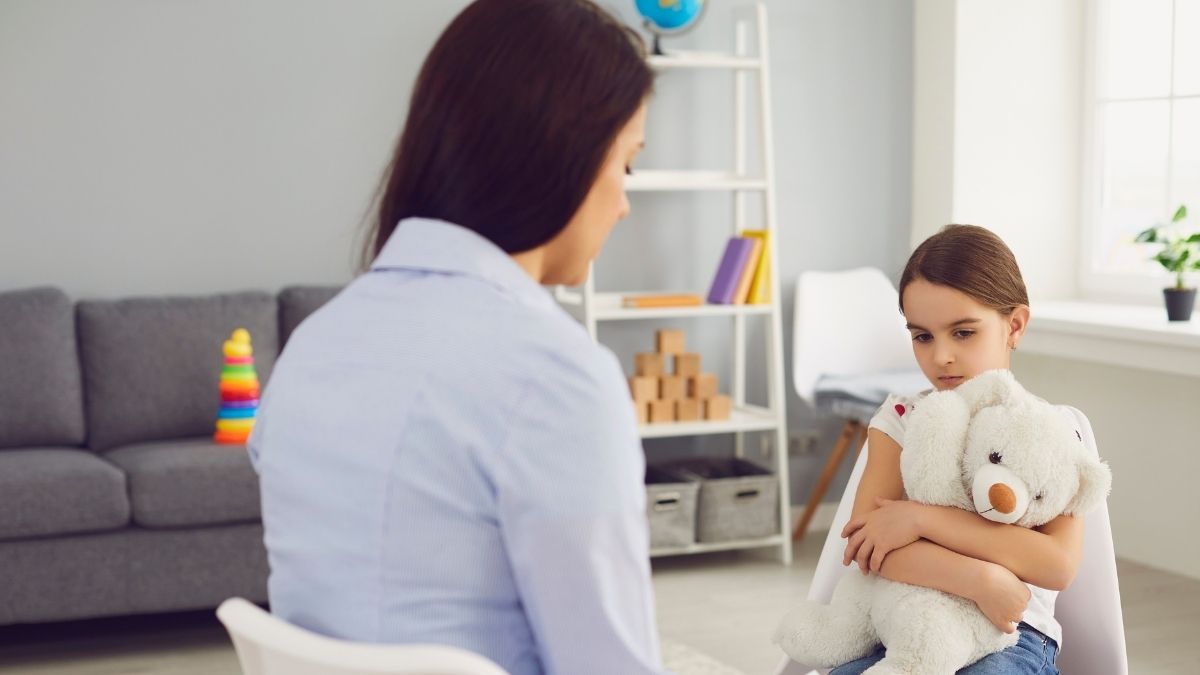 ABA therapist in NJ sitting with a young girl holding a teddy bear during a therapy session