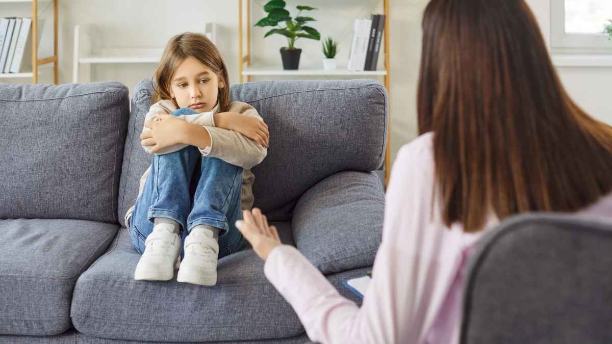Child sitting with arms crossed on couch as therapist answers common ABA therapy questions at home