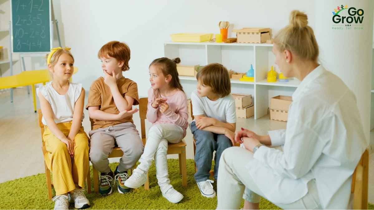 Four young children sitting in chairs engaging with a therapist in a bright classroom setting