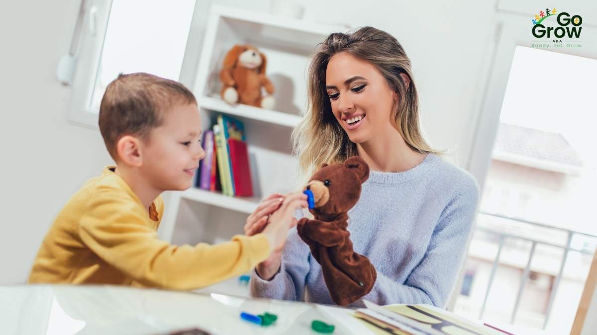 Smiling therapist engaging a young boy in play with a teddy bear during an in-home ABA session