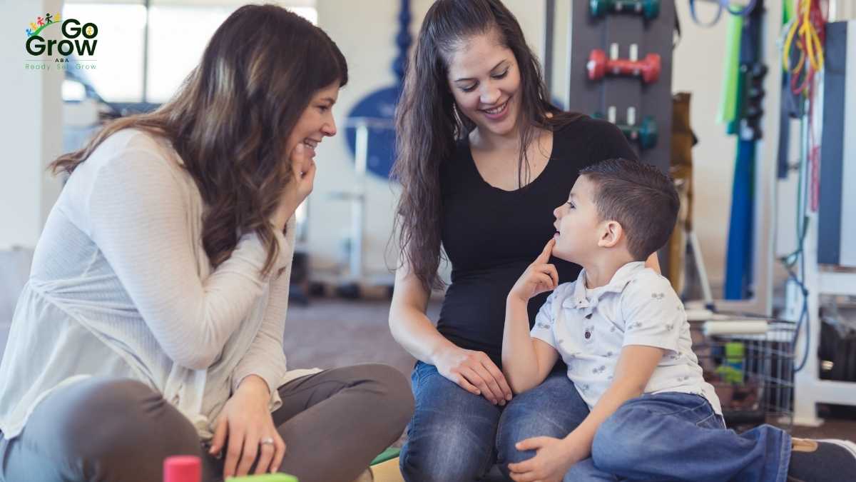 Two women smiling with a young boy sitting on one woman's lap during a therapy room interaction