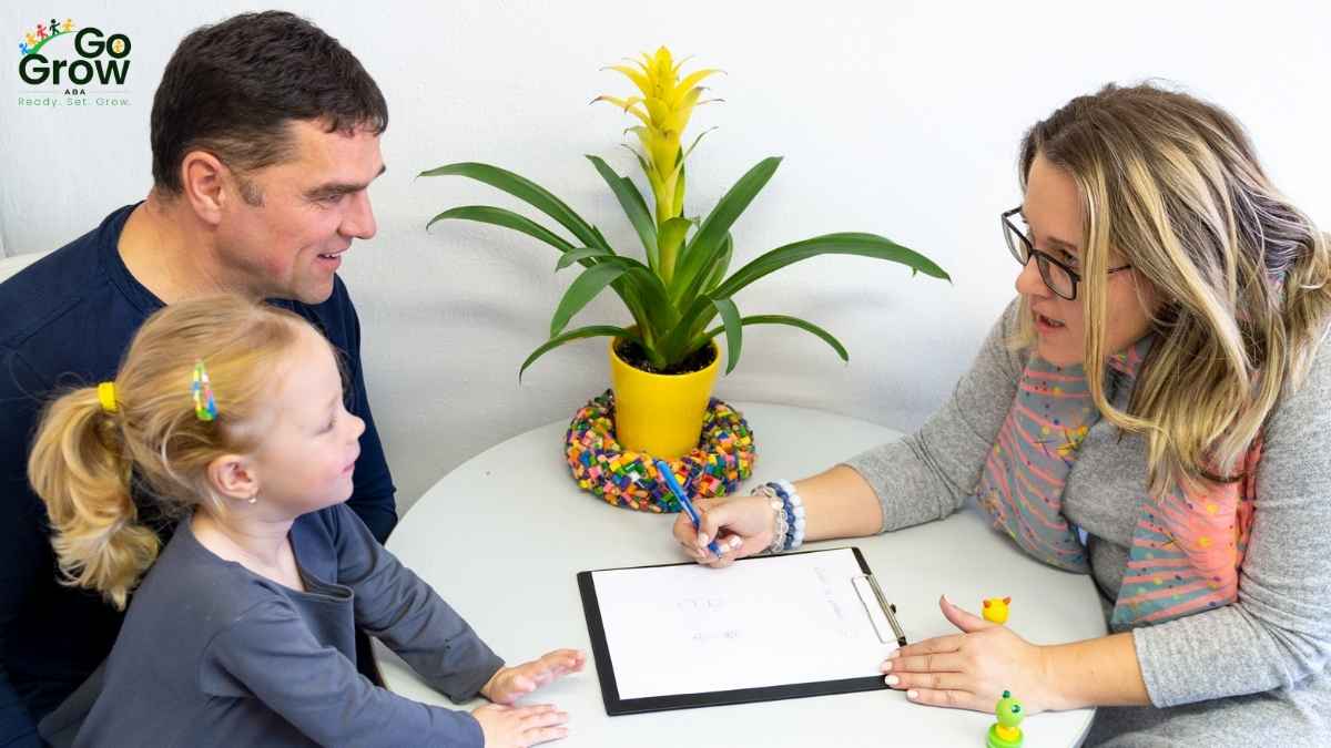 Father and young daughter sitting at a table while a clinician reviews notes on a clipboard